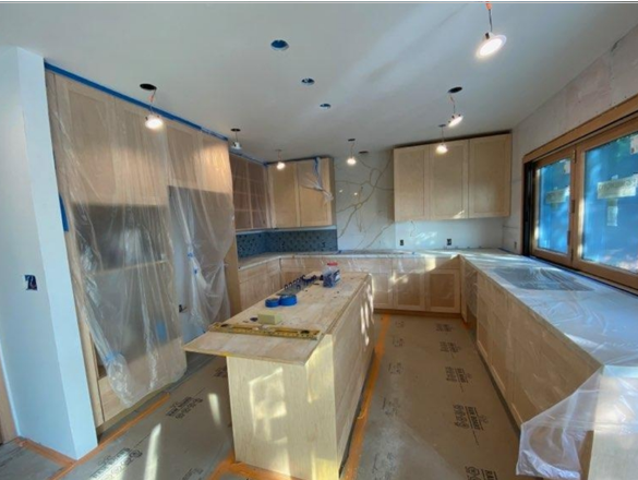 A kitchen under renovation with covered cabinets and construction lighting.