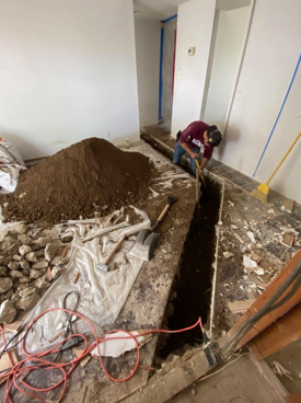 Construction worker trenching a foundation inside a home remodel project.
