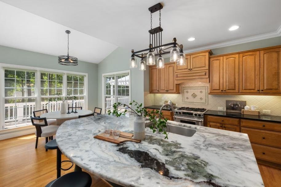 Spacious kitchen with a curved marble island, warm wood cabinetry, and large windows.